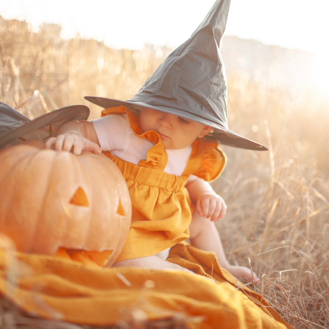 child in witch outfit next to pumpkin