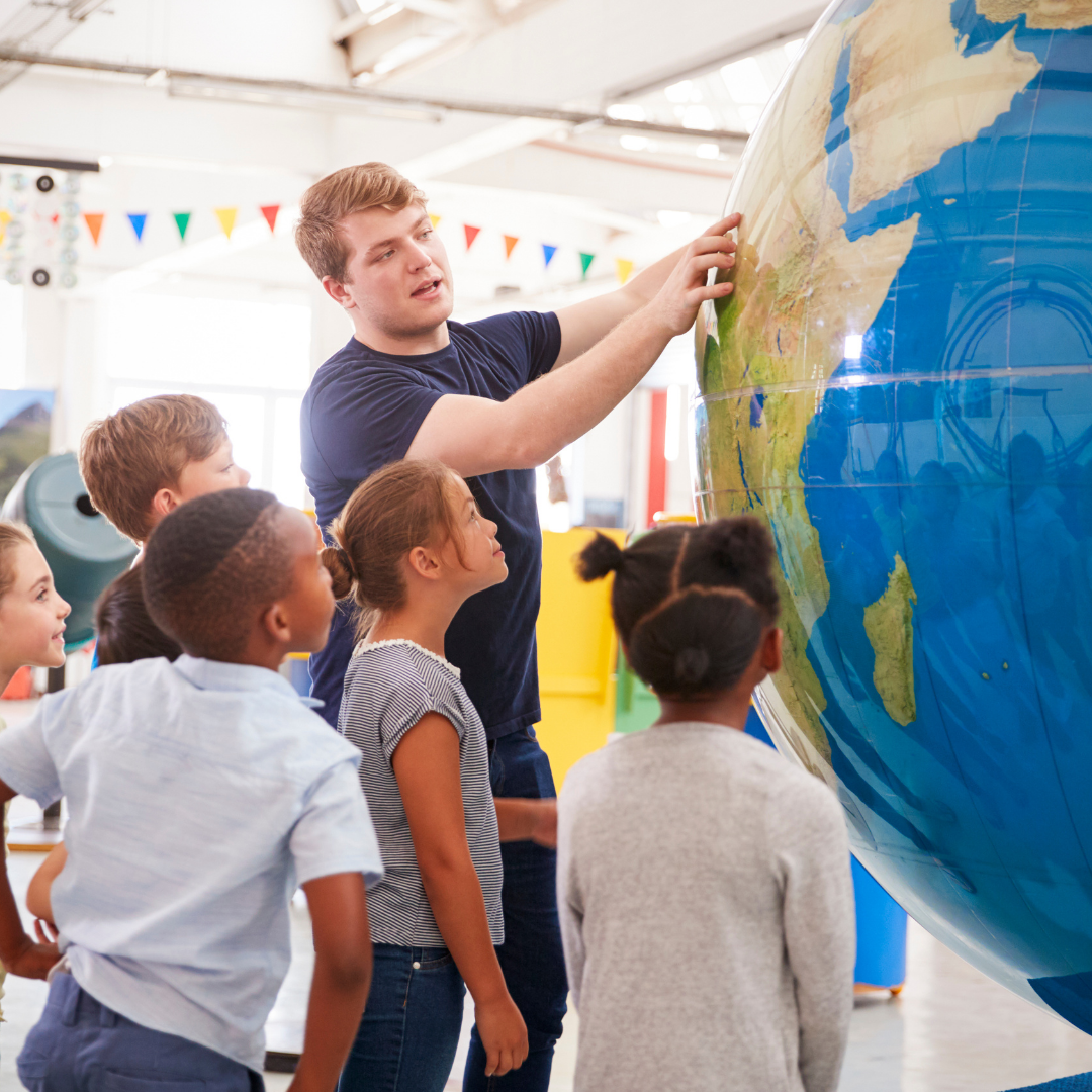 teacher pointing at a globe while kids are looking at him