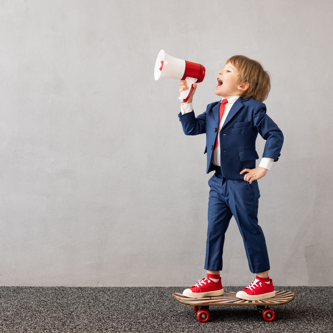A child standing on a skateboard in a suit and holding a microphone