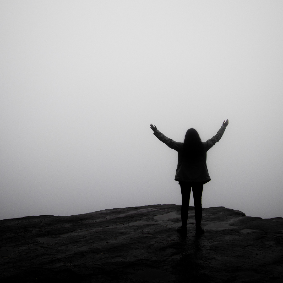 person with arms up and looking over cloudy edge
