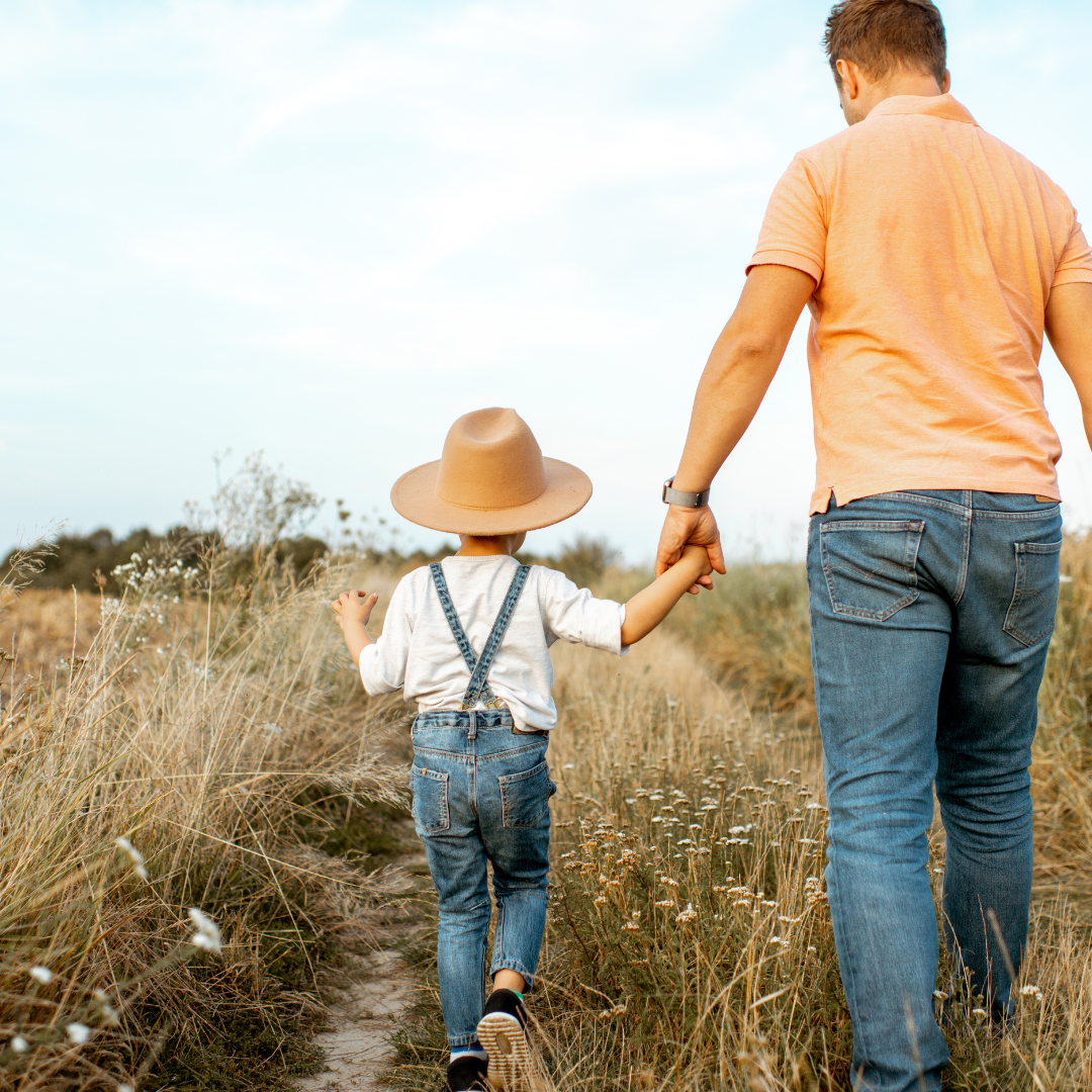 child and dad holding hands walking through a crop field