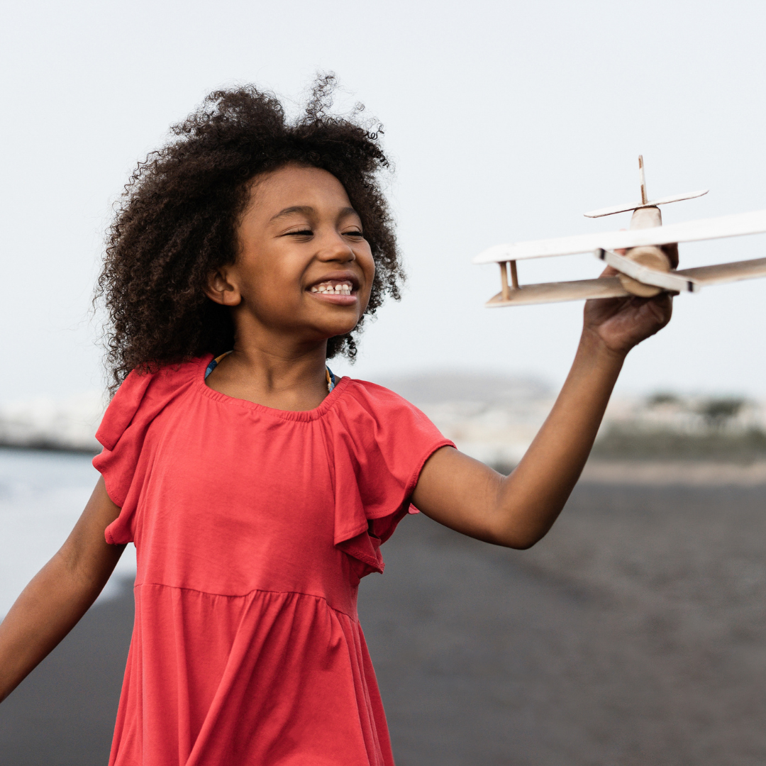 Little girl running on beach holding a play airplane